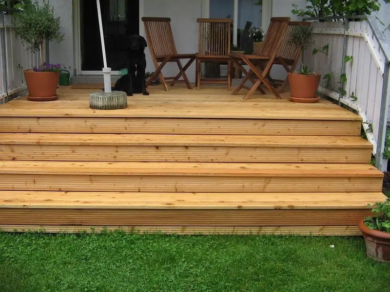 Holzterrasse mit breiten Stufen zum Rasen, darauf Stühle und Pflanzgefäße